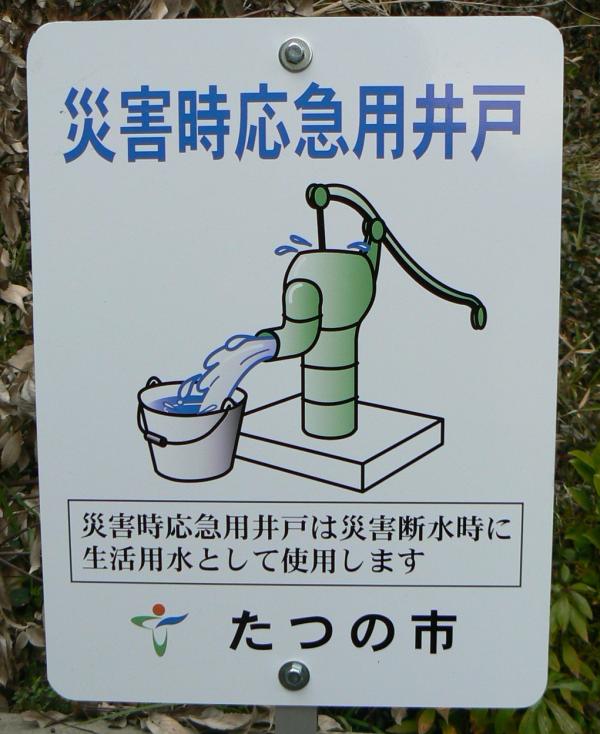 災害時応急用井戸と青い文字で書かれた手漕ぎの水汲み機のイラストの描かれた看板の写真