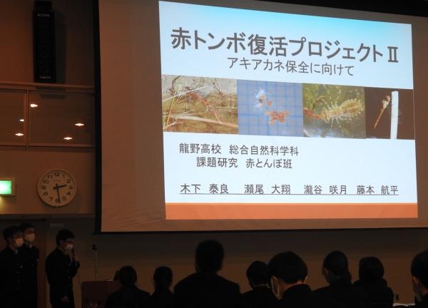 赤トンボ復活プロジェクト2とスクリーンに映された資料を使って横に立ち話をしている学生たちの写真