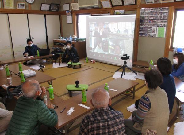 対話の糸に参加した方々が、広い畳の部屋に集まって大きなスクリーンに映される映像を観ている写真