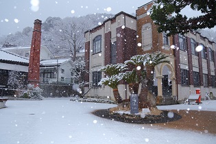 レンガで建てられた煙突がある建物周辺に雪が降り積もっている写真
