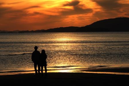 夕日に照らされた新舞子の海と浜辺に佇む二人の後ろ姿を写した作品