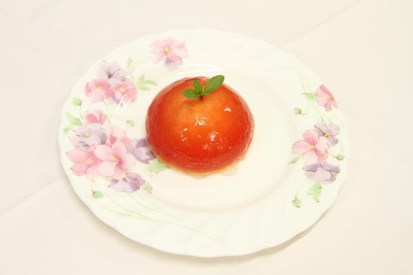 淡い花柄のお皿に、丸いトマトの中央に葉が付けらた艶やかな丸ごとトマトチーズケーキの写真