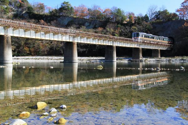 揖保川にかけられた鉄道の橋、川岸のトンネルから出てきてその橋の上を走る列車、浅い揖保川の水面に映された鉄道の橋と列車を斜め下から写した作品