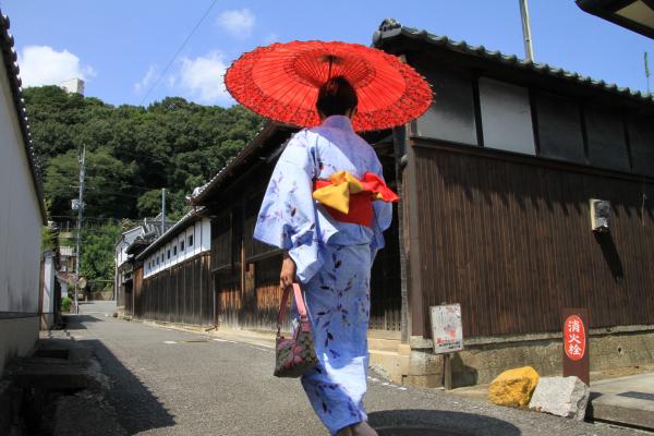 赤い和傘をさして城下町を歩く浴衣姿の女性の後ろ姿を斜め下から写した作品