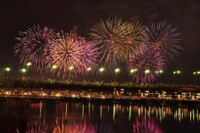 川岸から打ち上げられたいくつもの大輪の花火と、たくさんの何かの明かりがともった川岸を写した写真