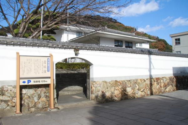 入口部分がくりぬかれた石垣と白壁の塀と、その塀の中に建つ白壁の立派な建物が写された写真