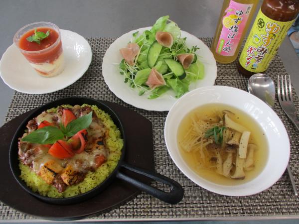 美味しそうなきのこ入りのスープや、生ハムが入ったサラダ、トマトを添えた焼きカレーのようなものなどがランチョンマットの上に並べられている写真