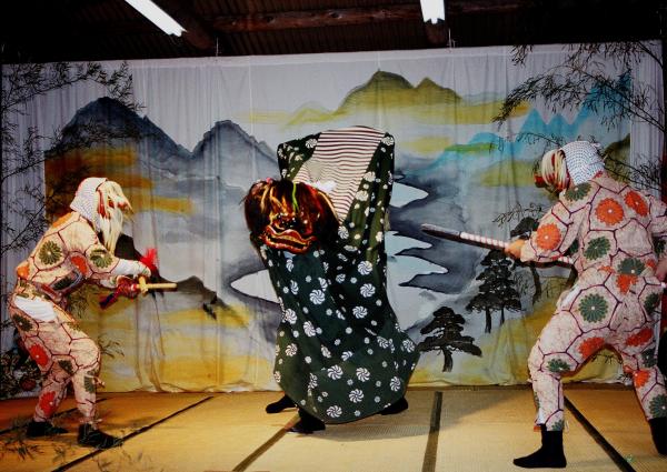 獅子頭と胴幕をつけて獅子舞を踊る人々と、天狗のお面をつけてその獅子に立ち向かう人々を写した写真
