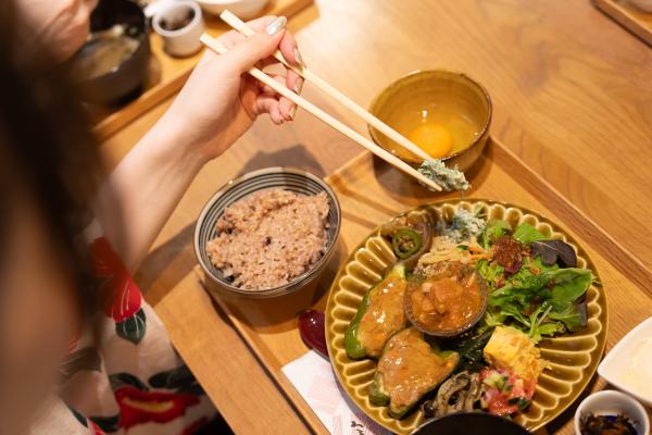 木製のトレイの上に野菜をふんだんに使用した地産地消ランチが置かれ、女性が食べている様子を上から撮影した写真