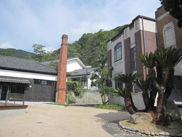 一本の長い赤レンガの煙突が併設された瓦屋根の建物と、その隣にあるレトロモダンな洋風の建物の写真