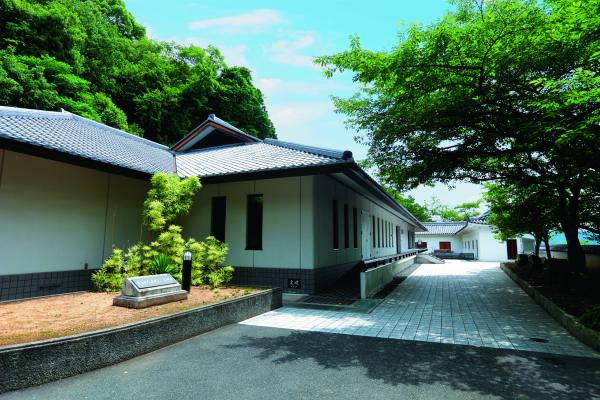 白い壁の大きな龍野歴史文化資料館の建物と、 その敷地内にたくさん植えられた緑の木々の写真
