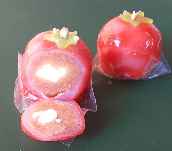 トマトの形をしたトマト餅が2つ置かれ、1つのトマト餅が切られ中のトマトあんとクリームチーズが見えている写真