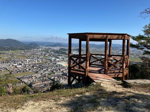 山頂にある屋根付きの木造の展望デッキとその山のふもとの街並みを写した写真