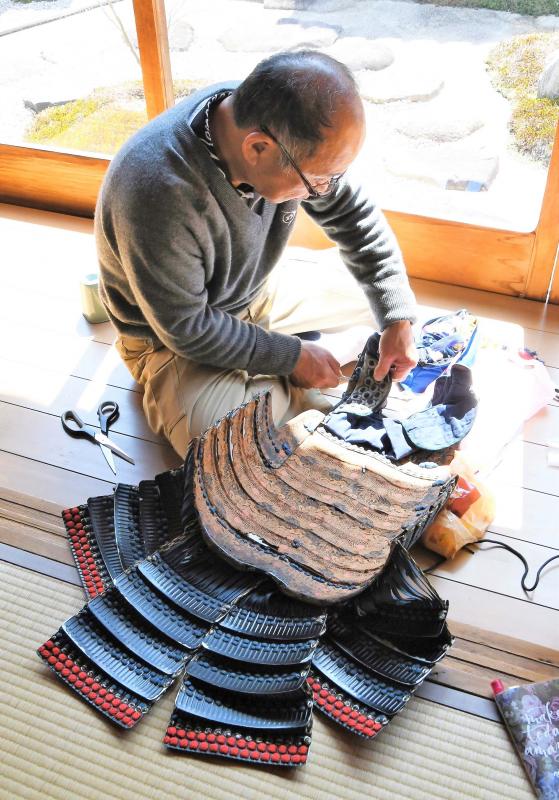 太陽の光がさす縁側に座って鎧を修理する男性の職人さんを斜め上から見下ろして写した作品