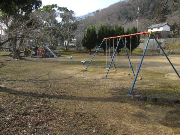 葉の落ちた木々の目立つ山々を背景に、広場にある滑り台やブランコの写真