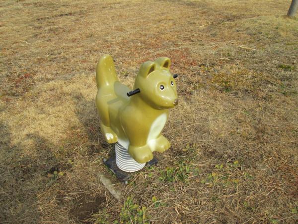 公園の芝生の上にある、黄土色のキツネのスプリング遊具の写真