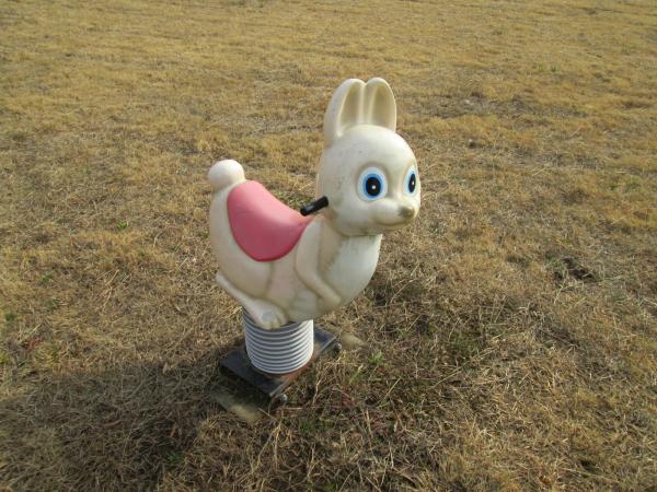 公園の芝生の上にある、白色のウサギのスプリング遊具の写真