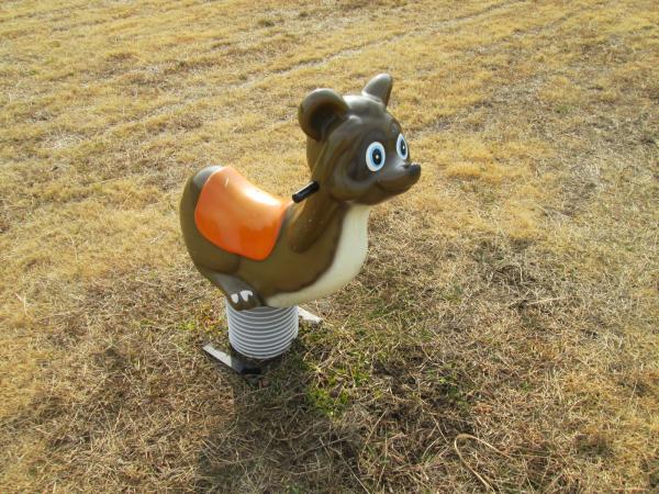 公園の芝生の上にある、茶色と白のタヌキのスプリング遊具の写真