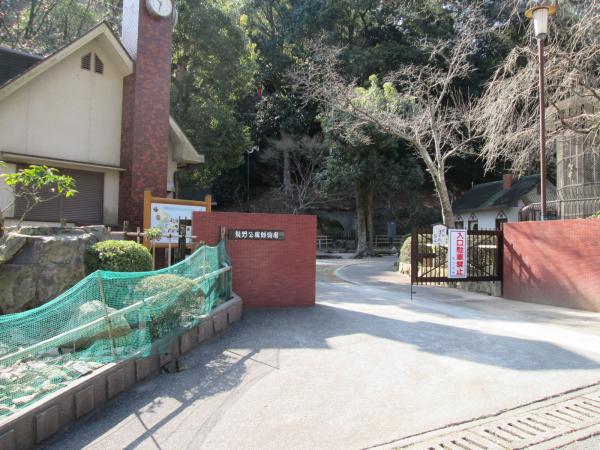 赤色のレンガの壁と正面玄関の黒い柵の奥に見える、木々と白い外観の建物が両端に2棟映る龍野公園動物園の写真