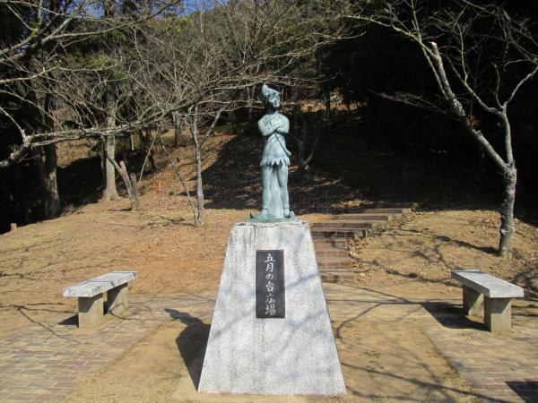 葉の落ちた木々の生えている広場にある、「5月の台広場」と彫られた台座の上に子どもの妖精のような銅像が設置されている写真