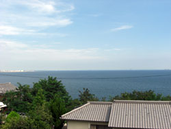 建物の屋根と緑の木々の向こうに見える海の写真