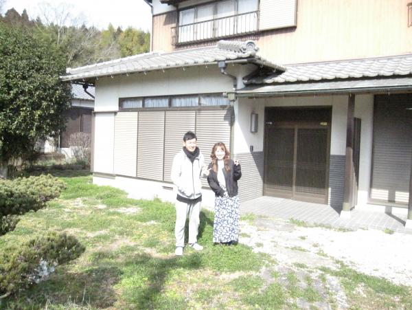 自宅の庭で笑顔で並んでピースをしているYさんご夫婦の写真