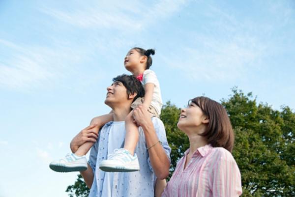 母親と、父親に肩車された小さな女の子が空を見上げている写真
