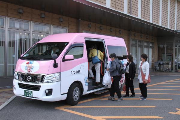 ピンクのボディが特徴的な市民乗り合いタクシー「あかねちゃん」に乗り込むお客さんを撮影した写真