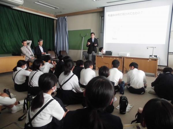 生徒達にスクリーンを見ながら説明をしている男性の写真