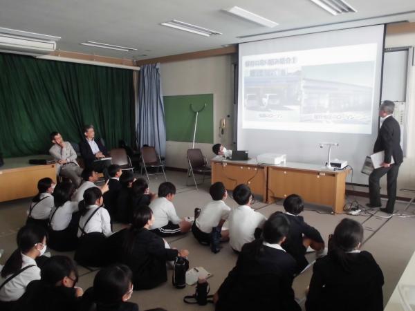 カーテンが閉められた室内でスクリーンに映った画面を見ながら床に座っている子どもたちの写真