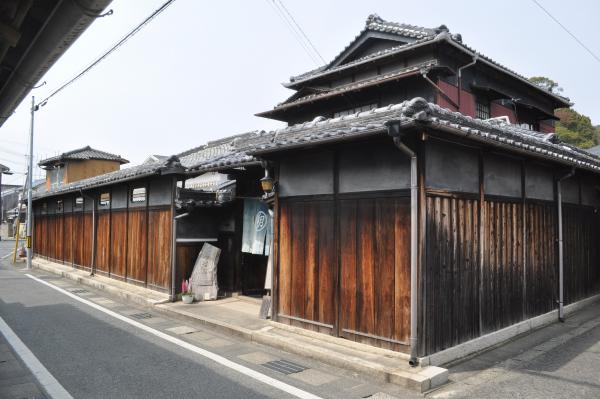 建物の周りが高い塀で囲われ、門には暖簾が飾られている屋敷型住宅の写真