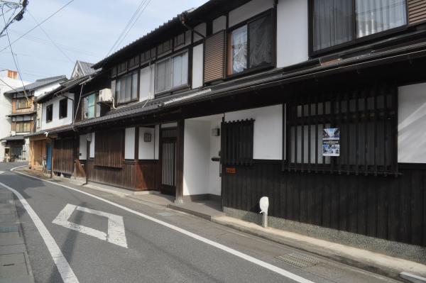 細い道路沿いに建つ建物の1階の窓に格子が設置された、白壁の古民家が建ち並ぶ川原町地区の写真