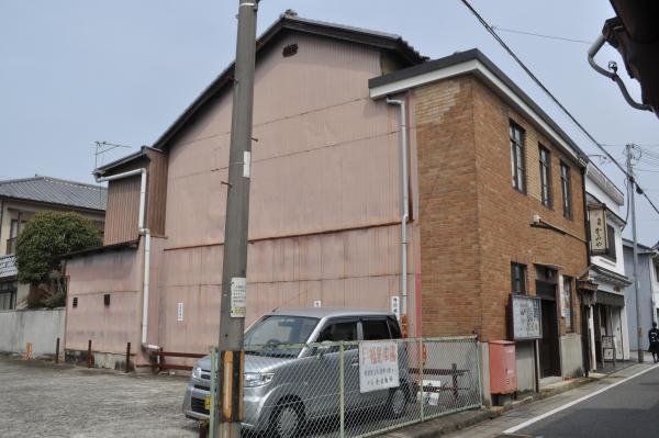 駐車場の奥に建つ高く外壁が茶色で大きな店舗のような看板がある建物の写真