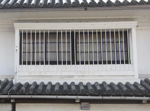 白の枠で囲まれた2階の窓に丸い格子がはめられている洋風な出格子の写真