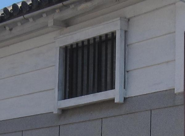 白い木枠に囲まれた窓枠に黒色の縦格子がはめられている木製の格子の写真