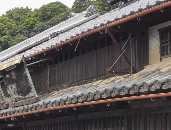 屋根の下の窓に黒の太い木と細い木の格子がはめられた木製出格子の写真