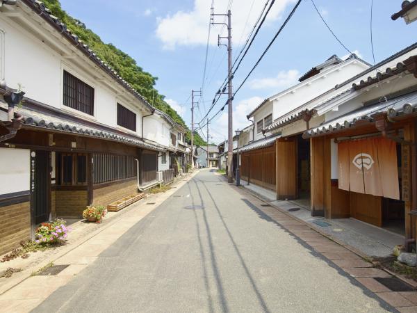 真っすぐに伸びた細い道路の右側の建物入り口に色褪せた暖簾がかかり、窓に格子が設置され白壁の建物が軒を連ねている門の外地区の写真