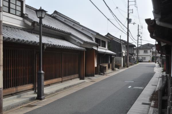 道路横に電灯が立ち、両側に木造の建物が並んでいる写真