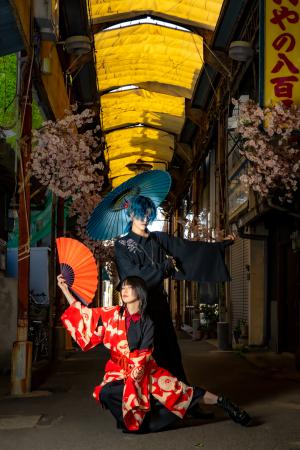 夜のシャッターが閉まった商店街で着物を着て青い和傘を持った男性とオレンジの扇子を持った女性がポーズをとって写っている写真