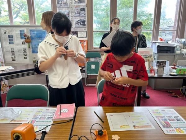 高校生と男子児童が立ってキーホルダーの金具を通している写真