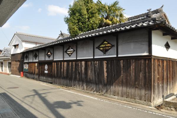 高い塀の下部に木材が使われ、上部は白壁の2色でひし形をした木材の窓がはめられ、塀の上には瓦が載っている塀瓦の高塀の写真