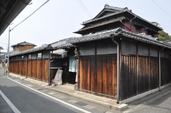 高い塀の下には木材が使われ、上は2色のグレー色で四角い形をした木材の窓がはめられ、塀の上には瓦が載っている塀瓦の高塀の写真
