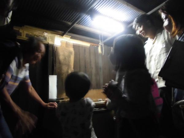 薄暗い麹室で店主の井戸さんの話を聞く参加者の子供2人と大人2人の写真