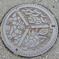町の花の梅、町の木やまもも、瀬戸内海の波と波頭を配した旧御津町のシンボルがデザインされたマンホールの写真