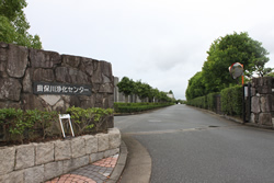 生垣や等間隔に配置された木々の間を真っすぐに伸びた通りを、乱形石の門に「揖保川浄化センター」と書かれた玄関から撮影した写真