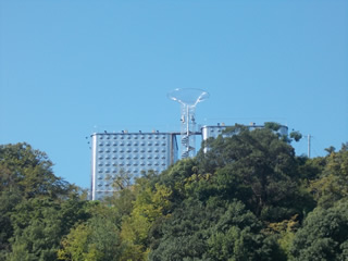 木々が鬱蒼と茂った林の奥に建つ、中央に巨大なろ過装置の様な物が設置された新宮配水池の建物の写真