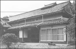 周囲に木々が立つ白壁の千本宿跡のモノクロ写真