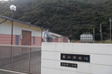 鬱蒼と茂った森の手前に、白とピンク色の外壁の香山浄水場の建物外観の写真