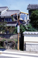 四角い二面の鏡がついたカーブミラーが、民家のそばの道路わきに設置されている写真