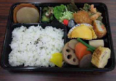 黒色の容器に煮物や揚げ物、サラダやご飯が盛り付けられた弁当の写真